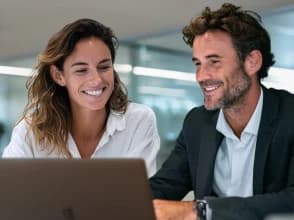 Two professionals collaborating and smiling while reviewing content on a laptop in an office.