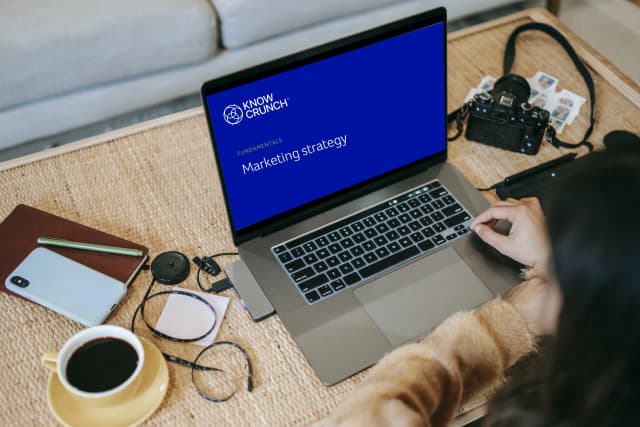 Laptop displaying a Knowcrunch marketing strategy fundamentals course on a desk with work accessories.