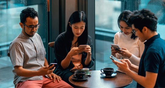 Two women and two men sit at a table and stare at their mobile phones.