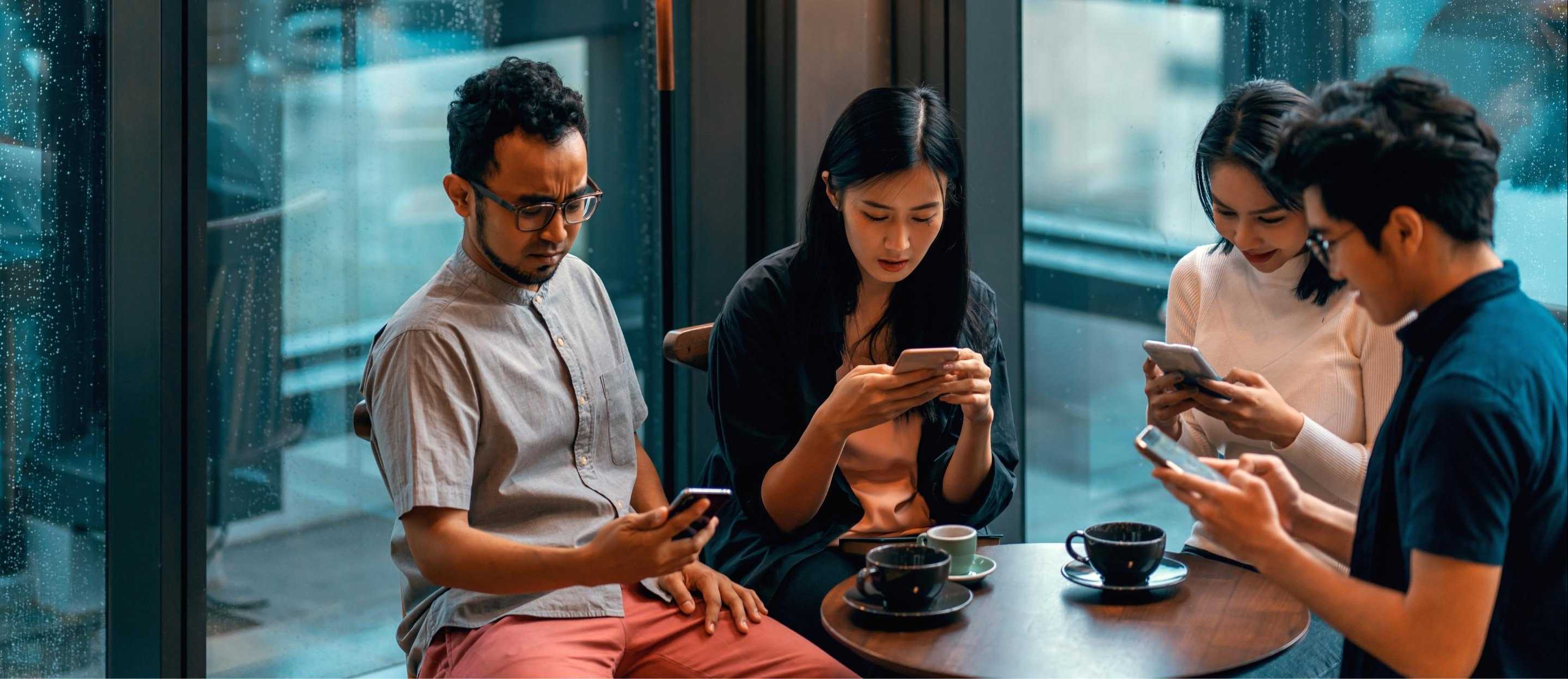 Two women and two men sit at a table and stare at their mobile phones.